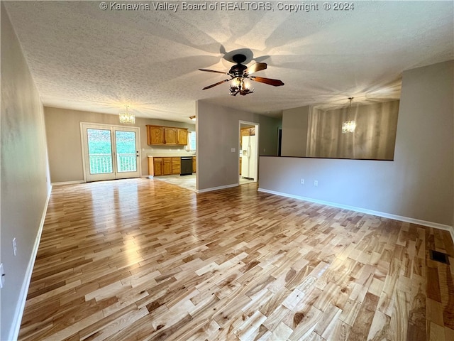 unfurnished living room with ceiling fan with notable chandelier, light wood-type flooring, and a textured ceiling