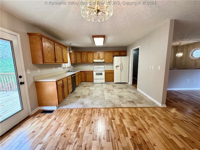 kitchen with sink, a notable chandelier, light hardwood / wood-style floors, decorative light fixtures, and white appliances