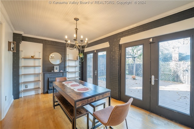 dining space with an inviting chandelier, french doors, light wood-type flooring, ornamental molding, and brick wall