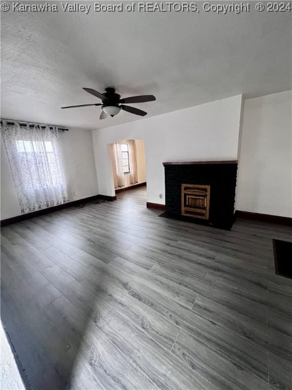 unfurnished living room featuring ceiling fan, dark hardwood / wood-style flooring, and a brick fireplace