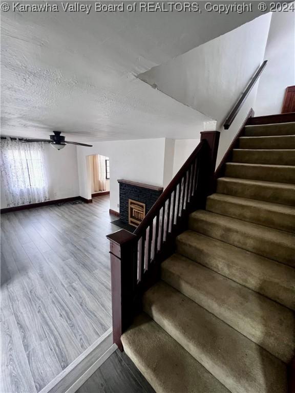 stairs with hardwood / wood-style flooring, ceiling fan, a textured ceiling, and a brick fireplace