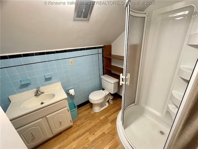 bathroom with hardwood / wood-style floors, toilet, vanity, a shower with shower door, and tile walls