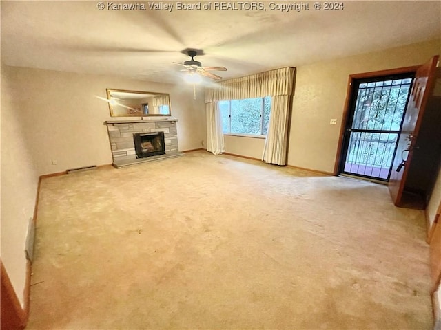 unfurnished living room with light carpet, a stone fireplace, and ceiling fan