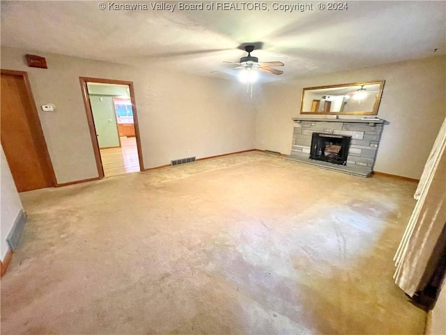 unfurnished living room with light colored carpet, a stone fireplace, and ceiling fan