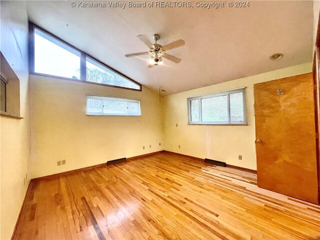 empty room featuring a healthy amount of sunlight, light wood-type flooring, and vaulted ceiling