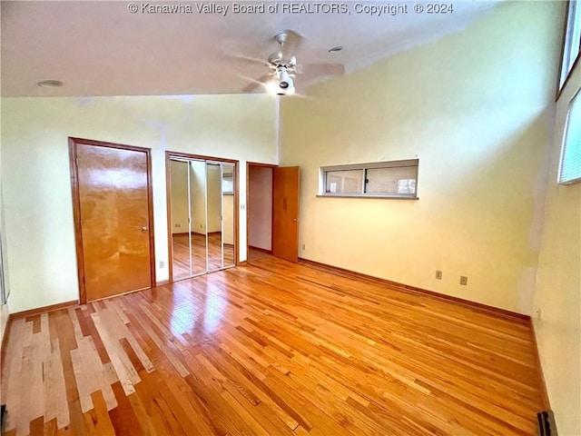 unfurnished bedroom featuring multiple closets, ceiling fan, light hardwood / wood-style flooring, and vaulted ceiling