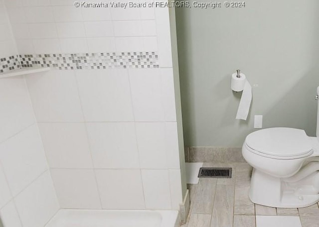 bathroom with tile patterned floors, a tile shower, and toilet