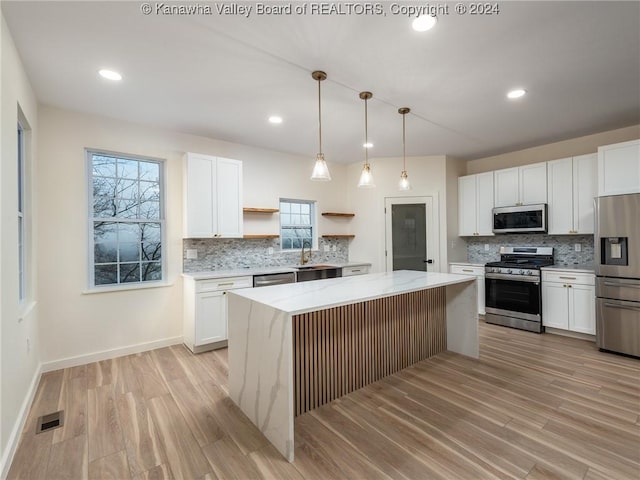 kitchen featuring white cabinets, appliances with stainless steel finishes, a center island, and plenty of natural light