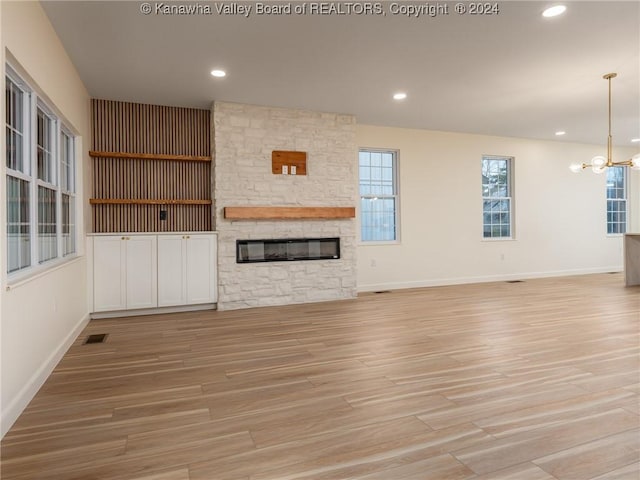 unfurnished living room with a stone fireplace, light hardwood / wood-style floors, and a notable chandelier