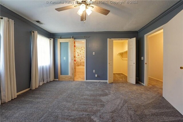 unfurnished bedroom with a walk in closet, crown molding, carpet flooring, ceiling fan, and a closet