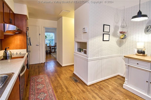 kitchen with stainless steel oven, pendant lighting, cooktop, and wood-type flooring