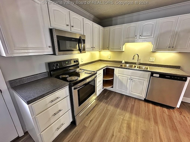 kitchen with white cabinetry, sink, stainless steel appliances, crown molding, and light hardwood / wood-style floors