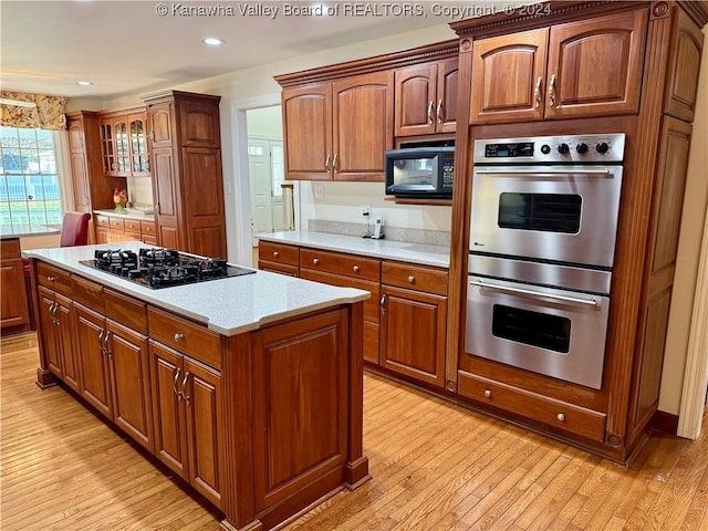 kitchen with light stone countertops, light wood-type flooring, a kitchen island, and black appliances