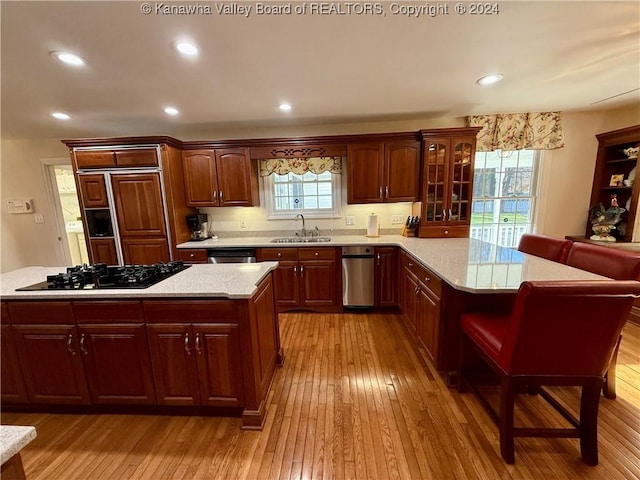 kitchen with light stone countertops, light wood-type flooring, black gas stovetop, sink, and a kitchen island