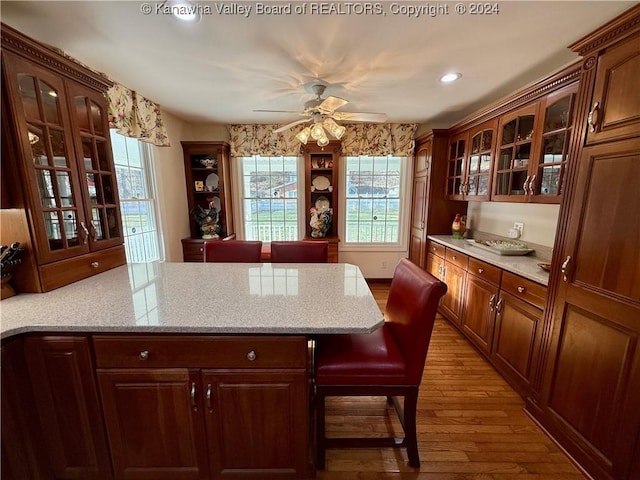 kitchen with hardwood / wood-style flooring, ceiling fan, light stone countertops, and a breakfast bar area