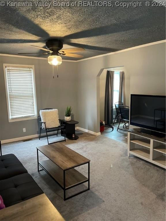 living room featuring carpet flooring, a textured ceiling, ceiling fan, and ornamental molding