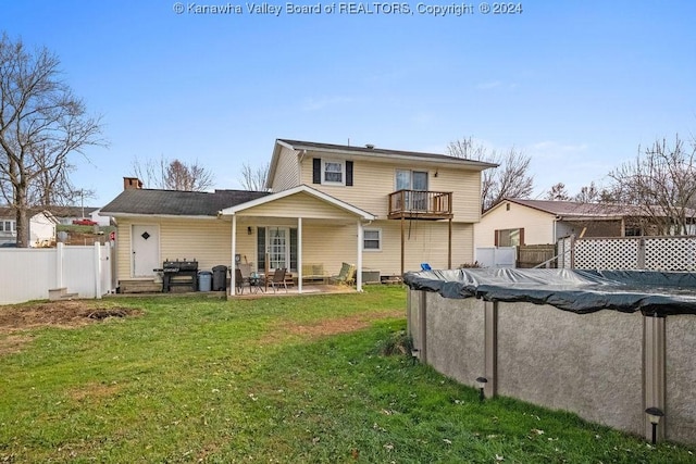 back of property with a balcony, a covered pool, a patio area, and a lawn