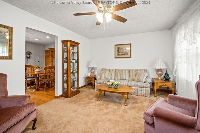 living room featuring ceiling fan, light colored carpet, and a textured ceiling