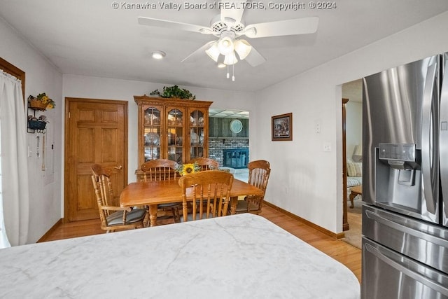 dining area with a fireplace, ceiling fan, and light hardwood / wood-style flooring