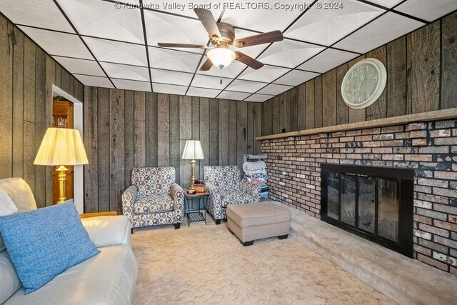 living room with a paneled ceiling, light carpet, wooden walls, and a fireplace