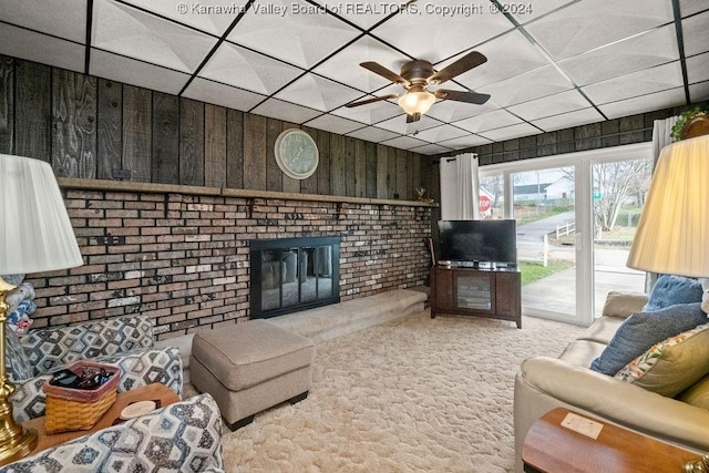 living room featuring a paneled ceiling, carpet floors, wooden walls, and a brick fireplace