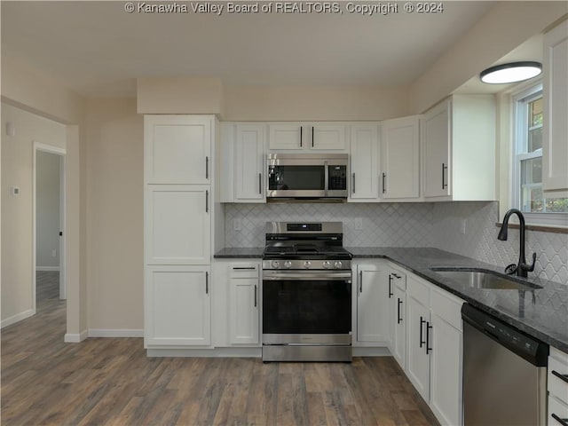 kitchen featuring stainless steel appliances, decorative backsplash, dark stone counters, white cabinets, and sink