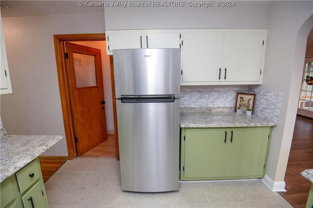 kitchen with backsplash, white cabinets, green cabinetry, light tile patterned flooring, and stainless steel refrigerator