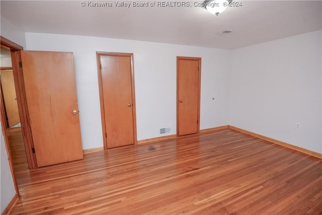 unfurnished bedroom with light hardwood / wood-style flooring and two closets