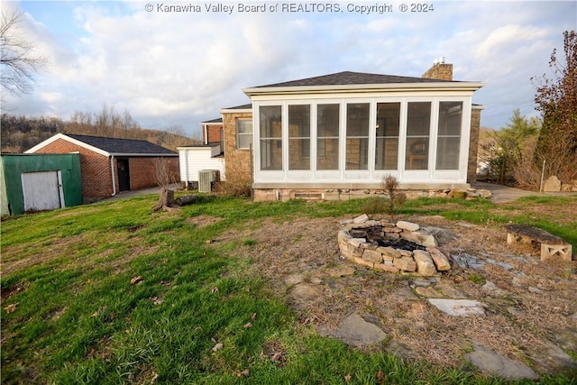 rear view of property featuring a sunroom, a fire pit, a lawn, and central air condition unit