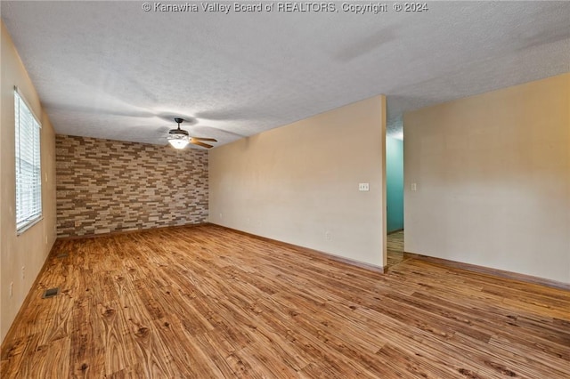 empty room with light wood-type flooring, a textured ceiling, and brick wall