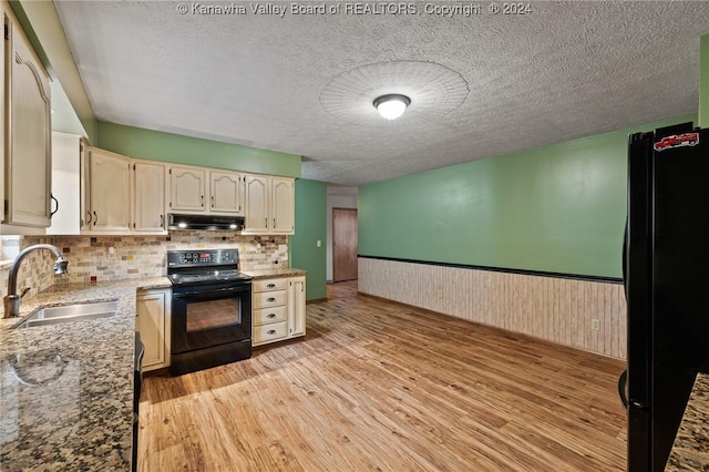 kitchen with wood walls, black appliances, sink, light wood-type flooring, and tasteful backsplash