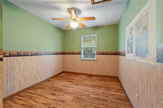 unfurnished room featuring wood walls, light hardwood / wood-style flooring, and ceiling fan