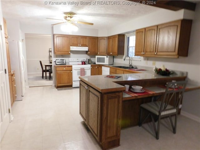 kitchen featuring kitchen peninsula, white appliances, ceiling fan, sink, and a breakfast bar area