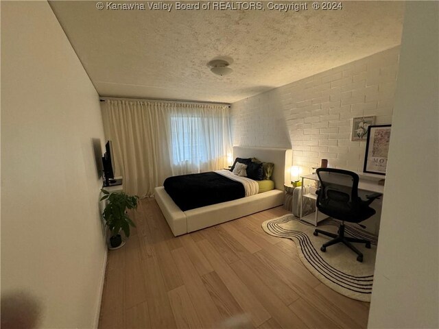 bedroom featuring brick wall, a textured ceiling, and hardwood / wood-style flooring