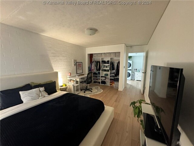 bedroom with a textured ceiling, light wood-type flooring, a closet, and brick wall