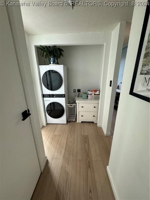 washroom with a textured ceiling, light wood-type flooring, and stacked washer / dryer