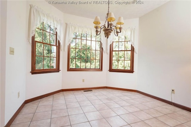 tiled spare room featuring plenty of natural light, a textured ceiling, and a chandelier