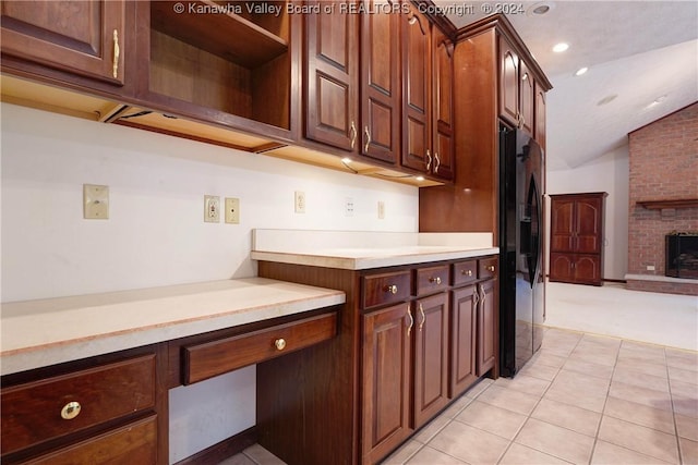 kitchen with black fridge, a brick fireplace, vaulted ceiling, light tile patterned floors, and dark brown cabinets