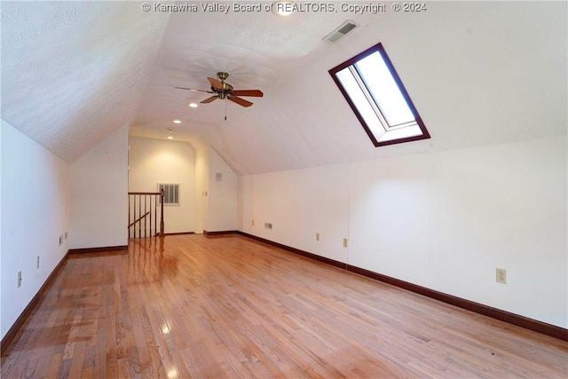 additional living space featuring ceiling fan, vaulted ceiling with skylight, light hardwood / wood-style floors, and a textured ceiling