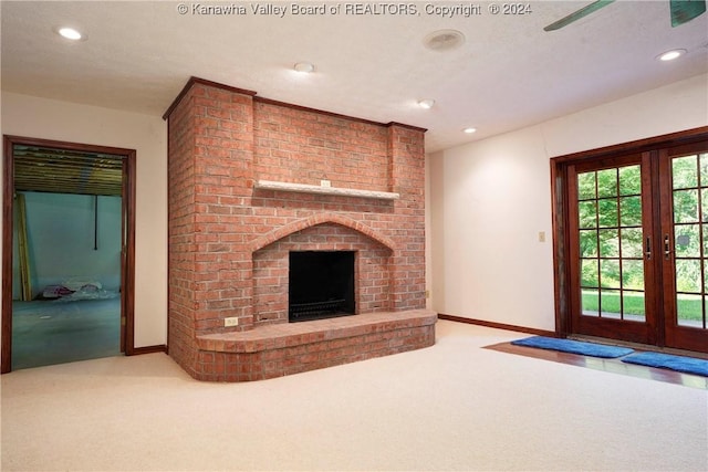 unfurnished living room featuring a textured ceiling, a fireplace, light carpet, and french doors