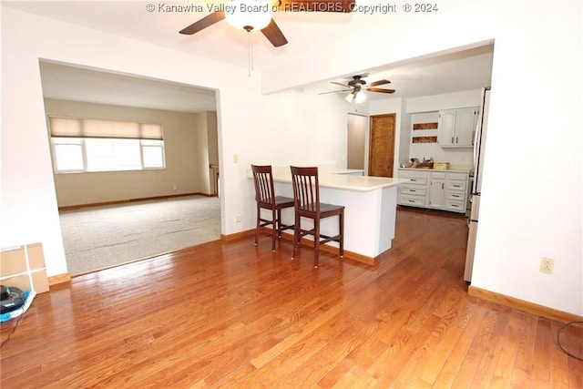 kitchen with kitchen peninsula, dark wood-type flooring, ceiling fan, and a breakfast bar area