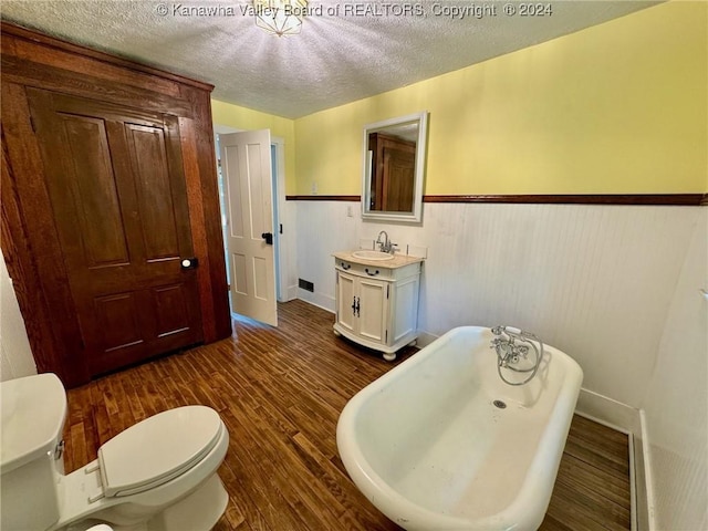 bathroom featuring a tub to relax in, vanity, a textured ceiling, wood-type flooring, and toilet