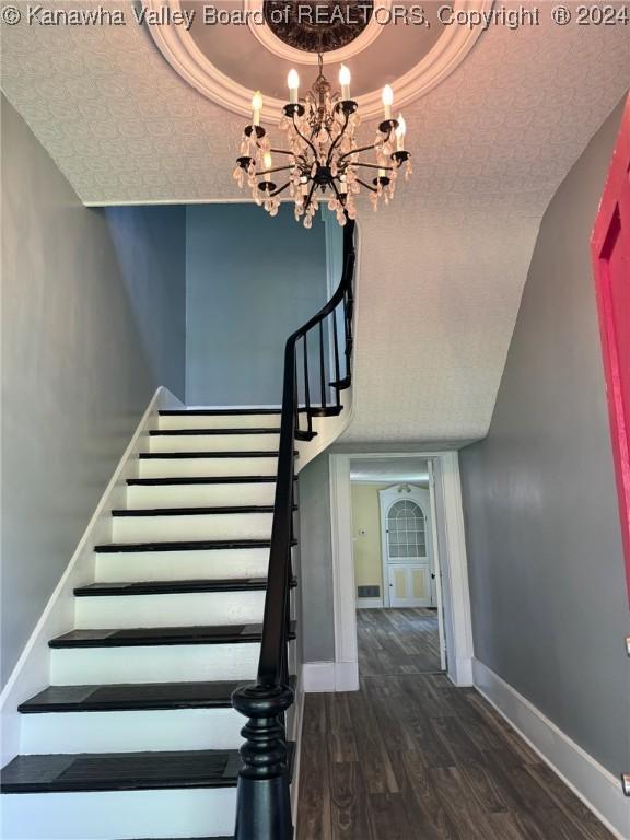 staircase with hardwood / wood-style floors, a raised ceiling, and an inviting chandelier