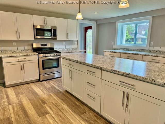 kitchen with white cabinets, hanging light fixtures, light stone countertops, light wood-type flooring, and appliances with stainless steel finishes