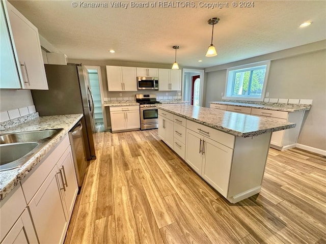 kitchen featuring hanging light fixtures, light hardwood / wood-style flooring, appliances with stainless steel finishes, a kitchen island, and white cabinetry