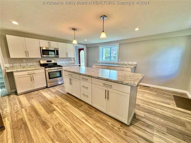 kitchen with stainless steel appliances, a kitchen island, pendant lighting, light hardwood / wood-style flooring, and white cabinetry