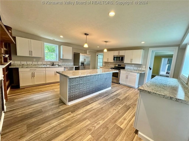 kitchen featuring pendant lighting, white cabinets, light hardwood / wood-style flooring, a kitchen island, and stainless steel appliances