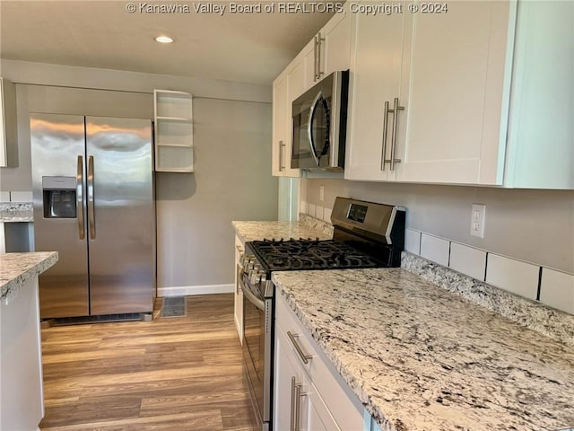 kitchen featuring white cabinets, light stone countertops, appliances with stainless steel finishes, and light hardwood / wood-style flooring