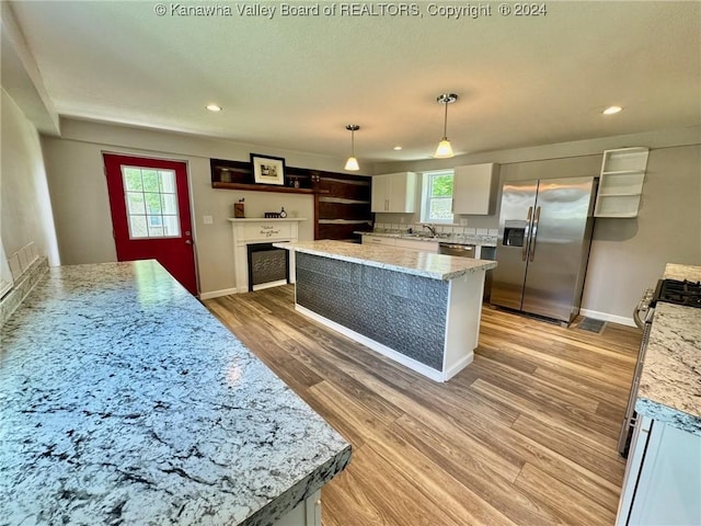 kitchen with light stone countertops, white cabinetry, a center island, hanging light fixtures, and appliances with stainless steel finishes