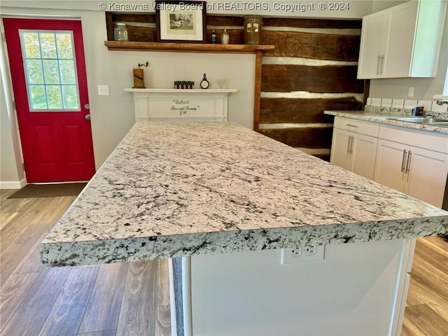 kitchen with a kitchen island, white cabinetry, sink, and light hardwood / wood-style flooring